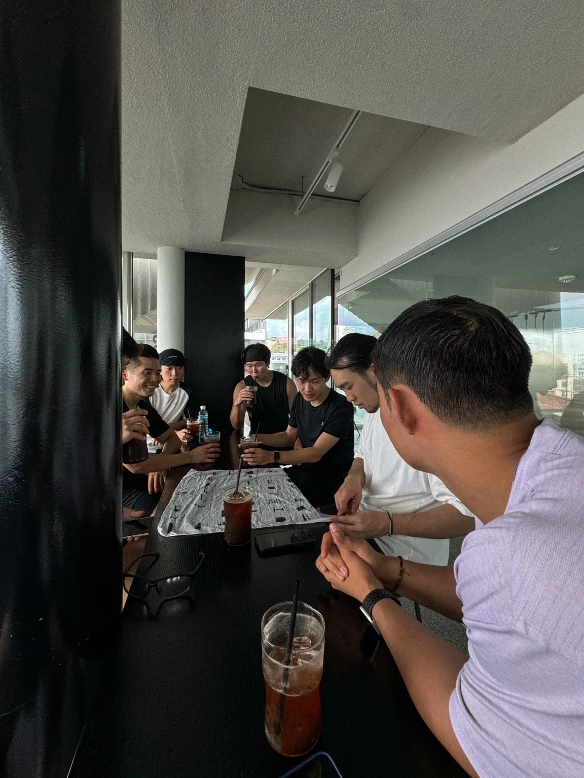 PMCC members sit around a long café table, holding iced coffees and talking after a run.